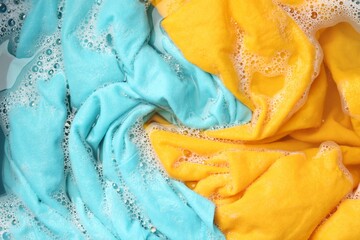 Colorful clothes soaked in water before washing, top view