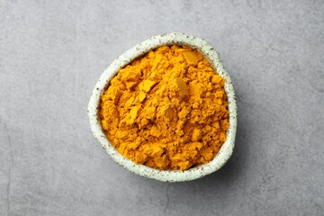 Turmeric powder in bowl on grey table, top view