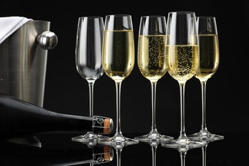 Bottle of sparkling wine, glasses and cooler bucket on black mirror surface