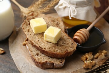 Slices of bread with butter, honey, milk and walnuts on wooden table, closeup