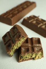 Pieces of tasty Dubai chocolate with pistachios and knafeh on white textured table, closeup
