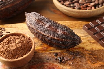 Cocoa pod, beans, powder and chocolate on wooden table, closeup