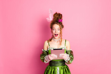 Young red-haired woman in baroque costume holding a tablet on a vivid pink background.