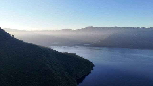 Vista a&eacute;rea de lago entre monta&ntilde;as con neblina matutina en las tierras altas.
