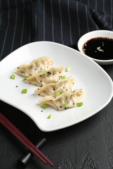 Delicious gyoza dumplings with chives and sesame seeds served on black table, closeup