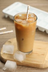 Refreshing coffee with ice and milk in glass on wooden table, closeup