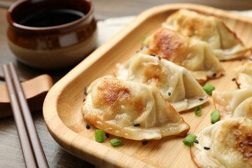 Delicious fried gyoza dumplings with sesame seeds served on wooden table, closeup