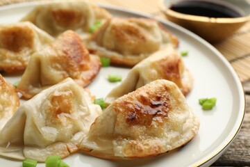 Delicious fried gyoza dumplings with green onions served on wooden table, closeup