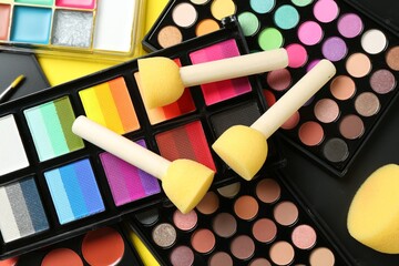Face paints, tools and makeup products on yellow background, closeup