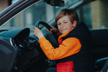 Child sitting on driver's seat and holding car steering wheel