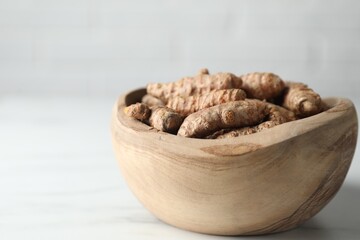 Raw turmeric roots in bowl on white table, closeup. Space for text