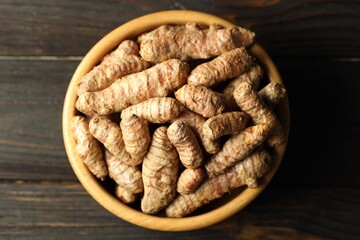 Tumeric rhizomes in bowl on wooden table, top view