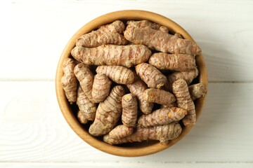 Tumeric rhizomes in bowl on white wooden table, top view