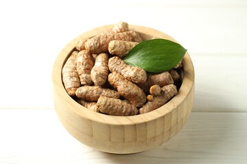 Tumeric rhizomes with leaf in bowl on white wooden table, closeup
