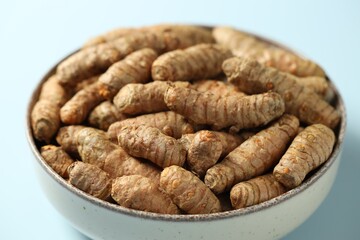 Tumeric rhizomes in bowl on light blue background, closeup
