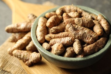 Tumeric rhizomes in bowl on grey table, closeup