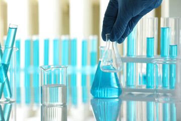 Woman with laboratory glassware at table indoors, closeup