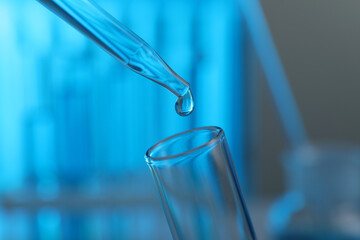 Dripping liquid into test tube on blurred background, closeup