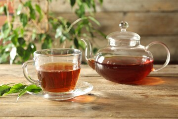 Freshly brewed tea in glass cup and teapot on wooden table