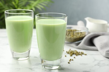Fresh mung bean juice in glasses and seeds on white marble table, closeup