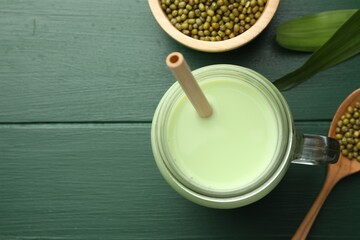 Fresh mung bean juice in mason jar, seeds and leaves on green wooden table, flat lay. Space for text