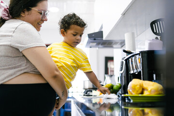 Pregnant mother holding her son while he is helping with chores in the kitchen
