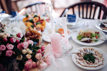 A close-up of a beautifully decorated wedding table with pink candles, fresh flowers, and delicious food including salads and meats.
