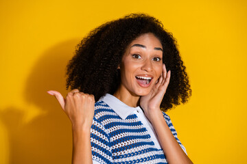 Happy young woman with curly hair and striped shirt gesturing enthusiastically against a vibrant...