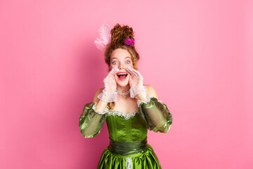 Elegant young woman in green period costume posing with enthusiasm against a pastel pink background