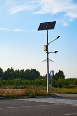 A solar-powered streetlight standing tall by a pedestrian crossing in a quiet, rural area.
