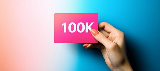 Woman s Hand Holding Pink Card Displaying 100K Celebration on Vibrant Blue and Pink Background