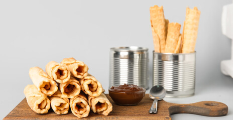 Board with stack of delicious wafer rolls on grey background