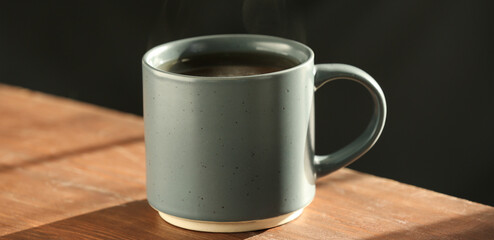 Green mug of hot tea on wooden table against dark background