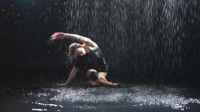 Contemporary woman dancer posing in rain water on black background. Female artist performer dancing with expression. Modern ballerina dancing in darkness. Passion dance in dark. Flexibility balance