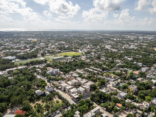 Aerial drone view of neighborhood with green areas in Tulum on a bright sunny day with blue cloudy sky 