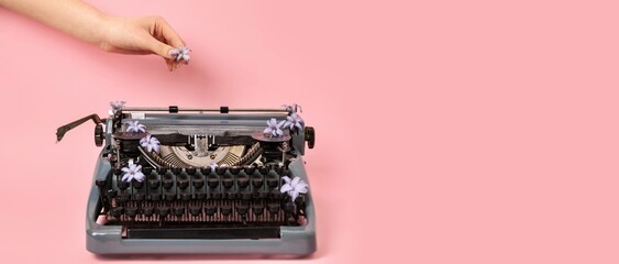 Woman's hand putting lilac flower on vintage typewriter against pink background with space for text