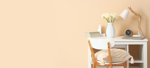 Workplace with ranunculus flowers in vase, laptop and lamp near beige wall. Banner for design