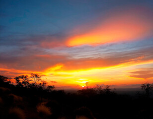 Bello atardecer con cielo naranja, amarillo, rojo y azul, sobre la montaña.