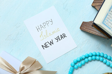 Card with text HAPPY ISLAMIC NEW YEAR, tasbih, gift box and Koran on color background