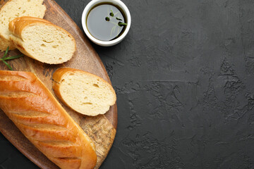 Cut fresh baguette with balsamic and rosemary on black table, top view. Space for text