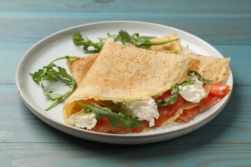 Delicious crepes with salmon, cream cheese and arugula on blue wooden table, closeup