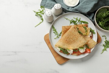 Delicious crepes with salmon, cream cheese and arugula on white marble table, flat lay. Space for text