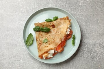 Delicious crepe with salmon, cream cheese and basil on grey table, top view