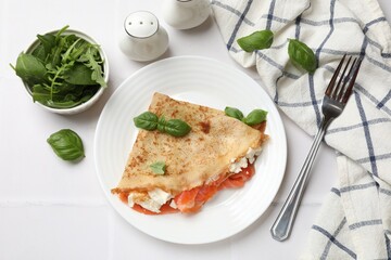 Delicious crepe with salmon, cream cheese, basil and arugula served on white tiled table, flat lay