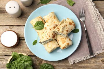 Tasty rolled crepes with cottage cheese and spinach served on wooden table, flat lay