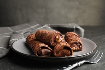 Delicious chocolate crepes with sweet paste and nuts on black table, closeup