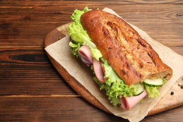 Delicious baguette sandwich with ham on wooden table, closeup