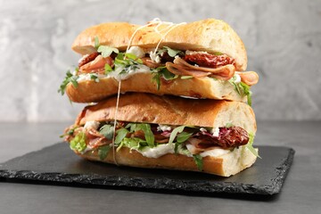 Halves of baguette sandwich with prosciutto and sun dried tomatoes on grey table, closeup