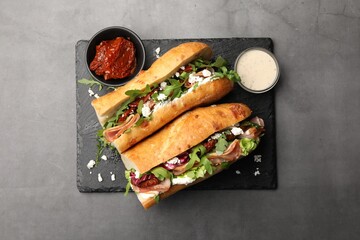 Halves of baguette sandwich with prosciutto and sun dried tomatoes served on grey table, top view