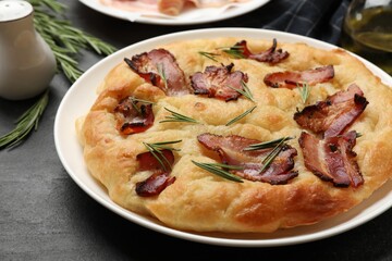 Delicious focaccia bread with bacon and rosemary on black table, closeup